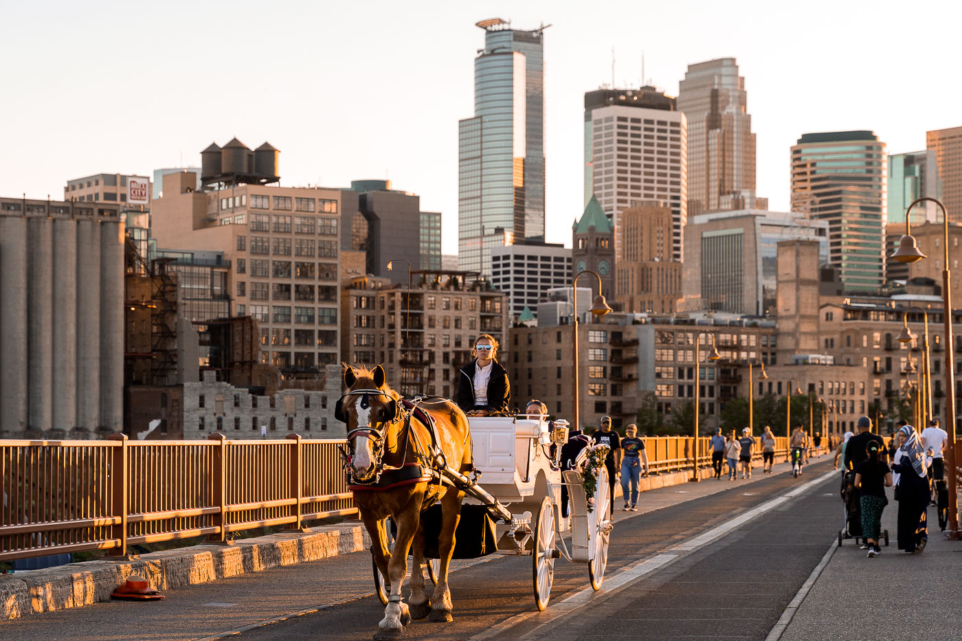 A horse-drawn carriage traverses the Stone Arch Bridge in Minneapolis, with the city's downtown skyline in the background. Constructed in 1883, the bridge originally served as a railway bridge for the Great Northern Railway before its conversion to a pedestrian and bicycle path, reopening in 1994. The bridge is a significant historical landmark offering views of the Mississippi River and the urban environment. It remains a popular destination for visitors and residents, providing a connection to Minneapolis's industrial heritage and its modern cityscape.