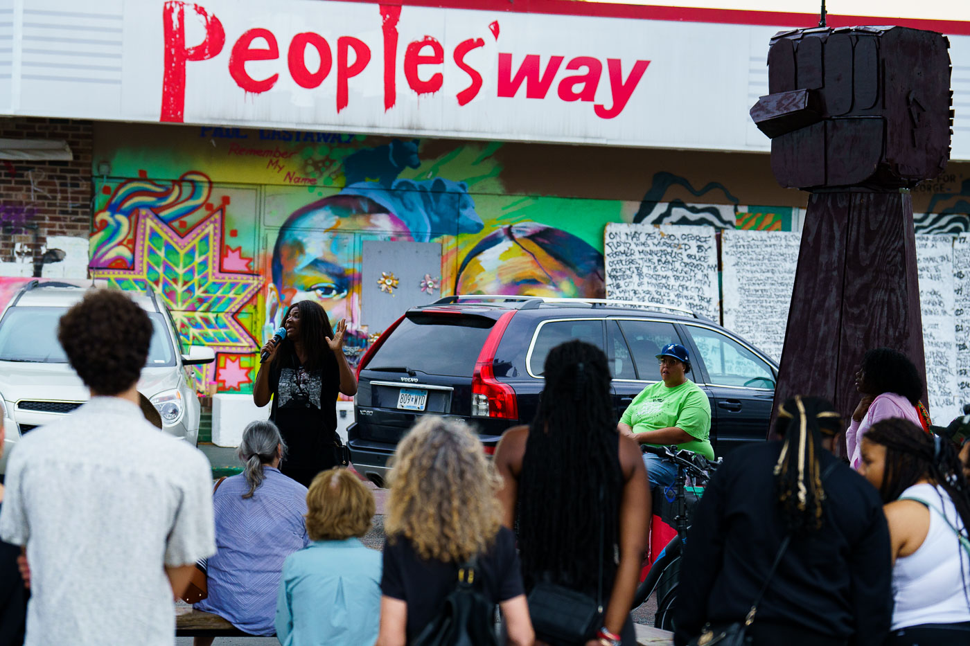 A rally for solidarity with Akron was held at George Floyd Square in Minneapolis, a site of ongoing protest and community organizing. Speakers, including George Floyd's aunt Angela Harrelson, addressed the crowd, expressing solidarity with Jayland Walker, who was killed by police in Akron, Ohio. Artists were present, working on a raised fist sculpture intended for Akron, symbolizing shared struggles. The event took place against a backdrop of murals and signage, including "People's Way," reflecting the area's significance.
