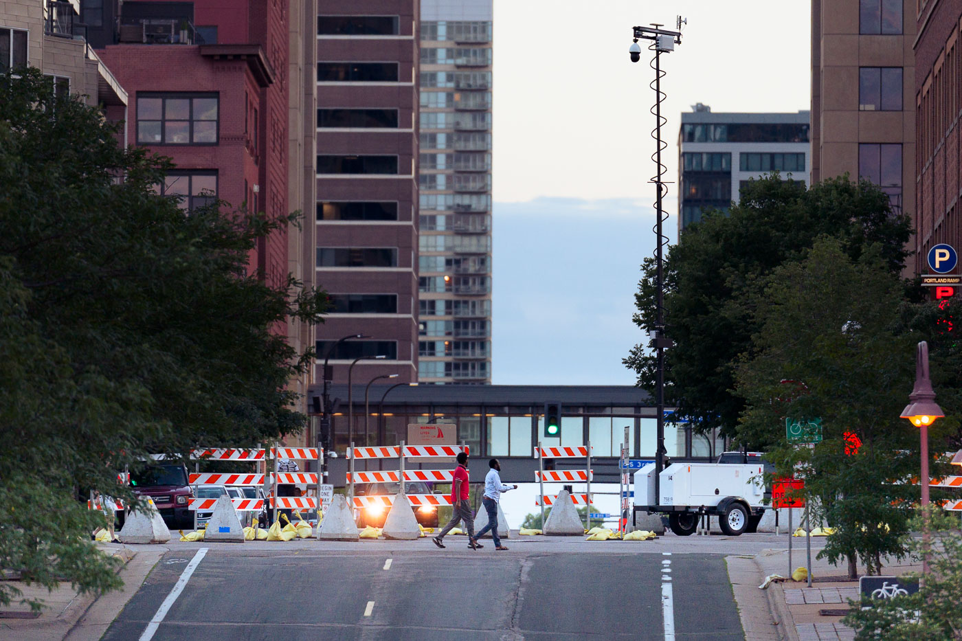 Concrete barriers and a surveillance camera are positioned in Minneapolis's Mill District, a measure reportedly implemented to deter "hot rodders." The presence of these security installations, alongside temporary construction barriers, indicates a response to concerns about public safety or unauthorized vehicle access. The Mill District, characterized by its historic industrial architecture and recent redevelopment, has also been a site of significant public events, including the Minneapolis Uprising, which may have influenced the deployment of such security infrastructure.