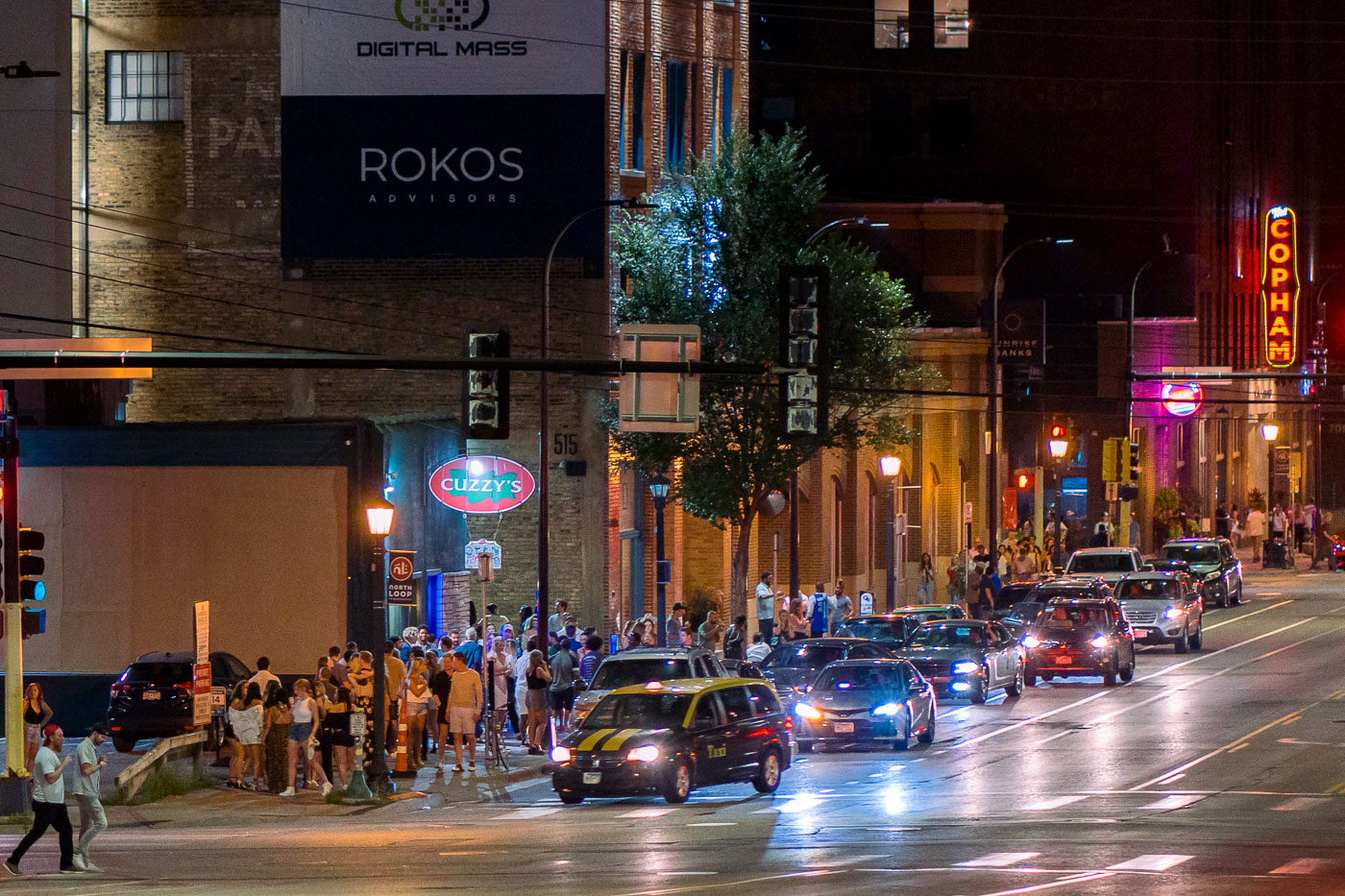 Washington Avenue in Minneapolis's North Loop district is a popular nightlife destination, as seen by the crowds gathered outside bars and establishments on a summer evening. The North Loop, historically a warehouse district, has transformed into a vibrant area for entertainment and dining, while retaining much of its early 20th-century industrial architecture. This street, a key artery in the neighborhood, bustles with activity, showcasing the area's contemporary appeal amidst buildings that speak to its past as a center for commerce and industry.