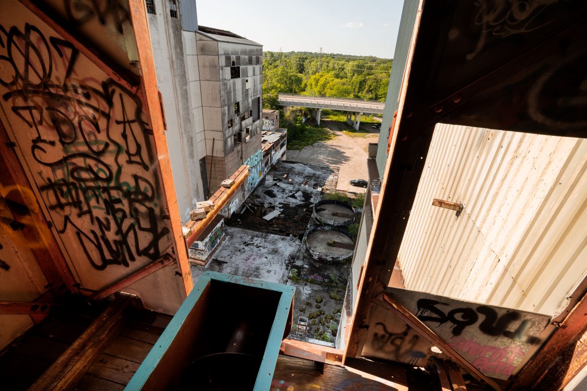 View through abandoned Fruen Mill interior showing graffitied metal surfaces, corrugated roofing, and forested landscape beyond.