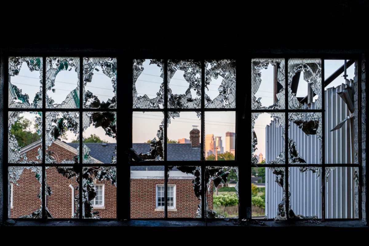 Broken windows with ivy frame the Minneapolis skyline through an abandoned industrial building.