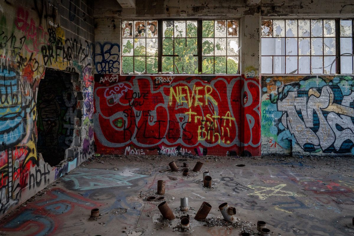 Abandoned Fruen Mill interior in Minneapolis with red graffiti wall, broken windows, and rusted metal floor studs.