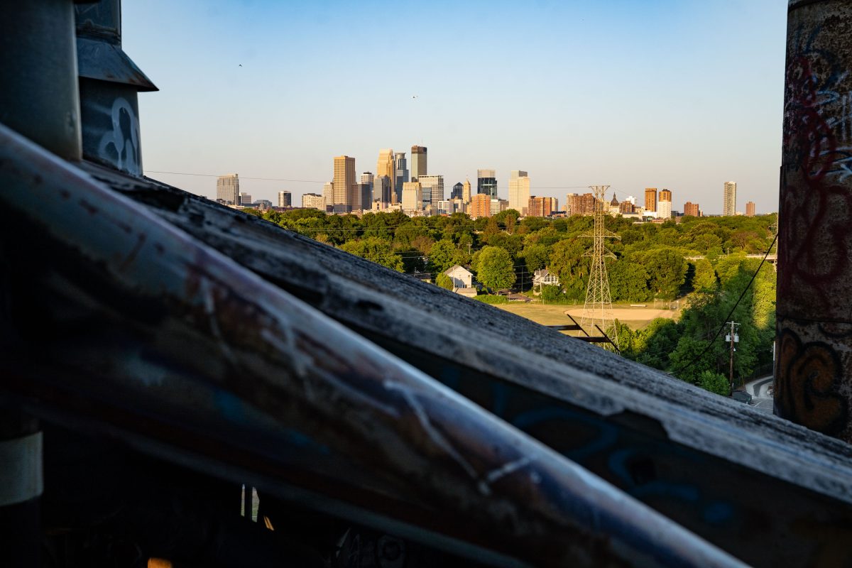 Minneapolis skyline visible beyond the Fruen Mill industrial structure and surrounding trees.
