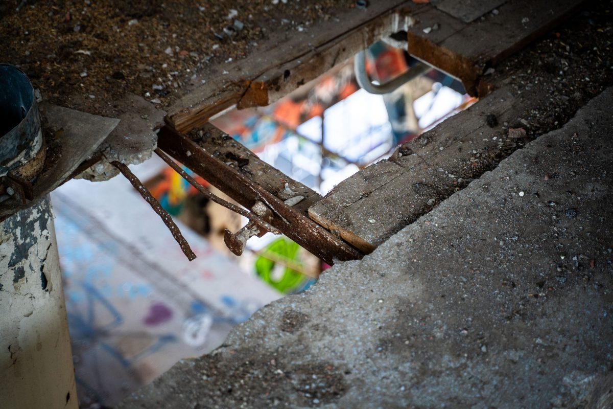 Rusted metal pulley and chains visible through a gap in the deteriorating floor of the abandoned Fruen Mill in Minneapolis.