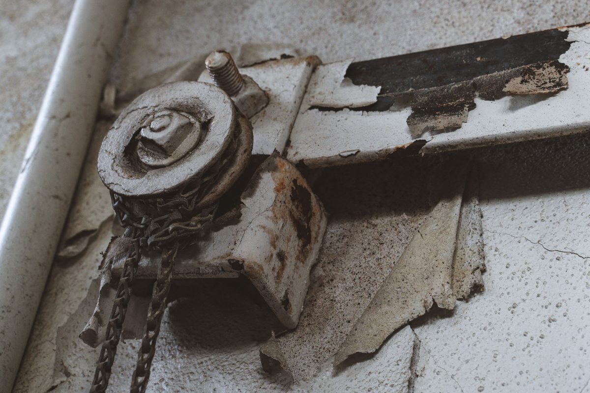 Rusted pulley and chain mechanism on deteriorating concrete surface inside abandoned Fruen Mill.