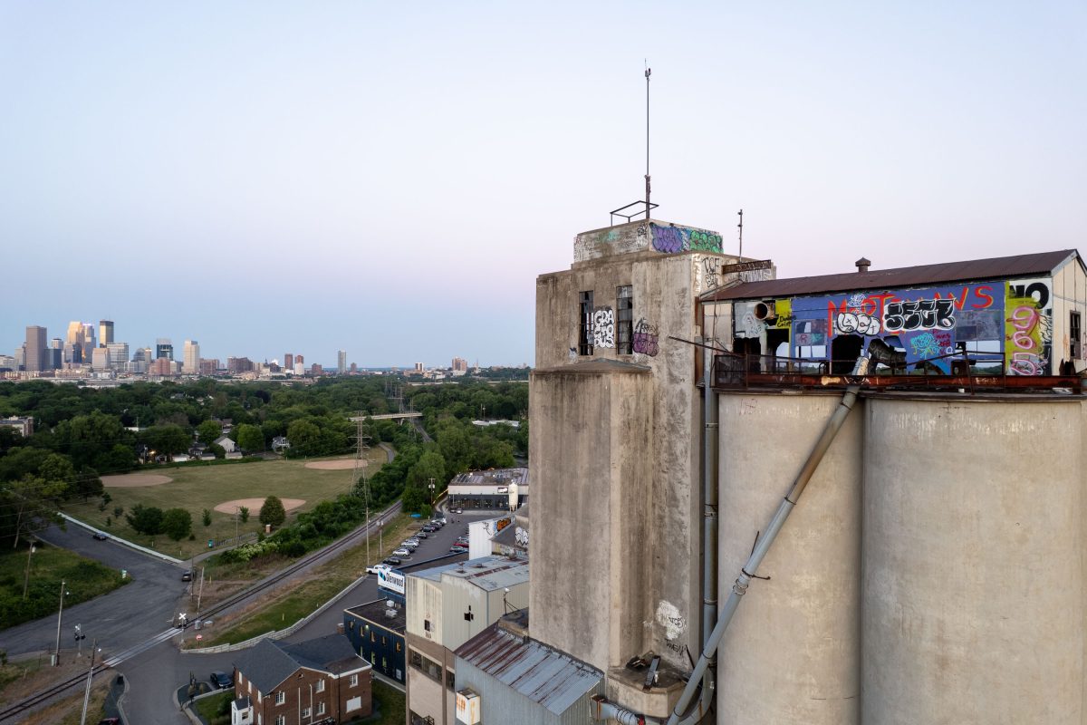 Rooftop of abandoned Fruen Mill in Minneapolis with colorful graffiti and downtown skyline visible beyond surrounding trees.