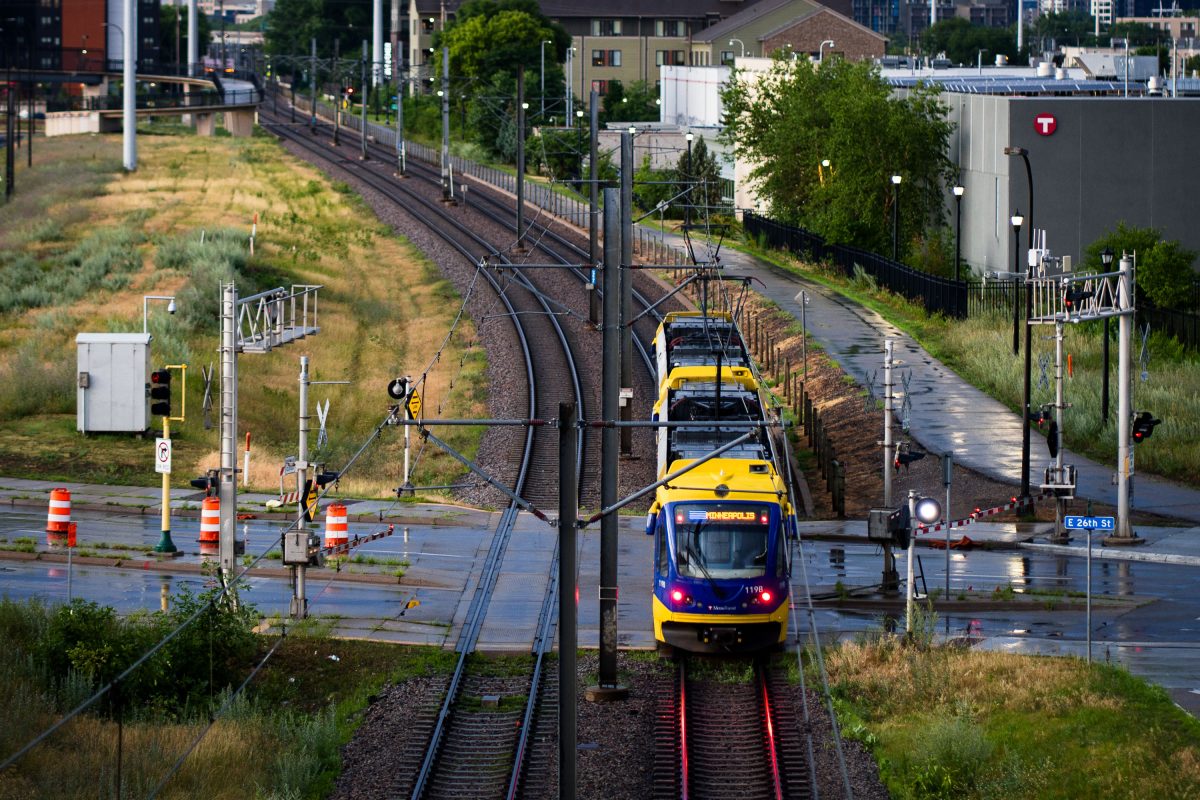 A yellow and blue METRO Blue Line light rail train approaches a street crossing near downtown Minneapolis.
