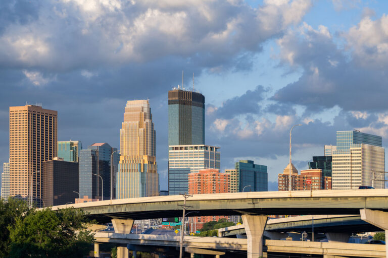 Minneapolis Skyline and I-35W Overpasses 1 The Minneapolis skyline rises behind the elevated overpasses of Interstate 35W, a major north-south freeway. This complex network of concrete structures, viewed from the Cedar Lake Trail, facilitates regional transportation and connects the city's central business district with surrounding areas. The construction of I-35W, completed in stages from the 1960s through the 1990s, significantly reshaped the urban environment and continues to serve as a vital artery for commerce and daily commutes in the Twin Cities metropolitan area.