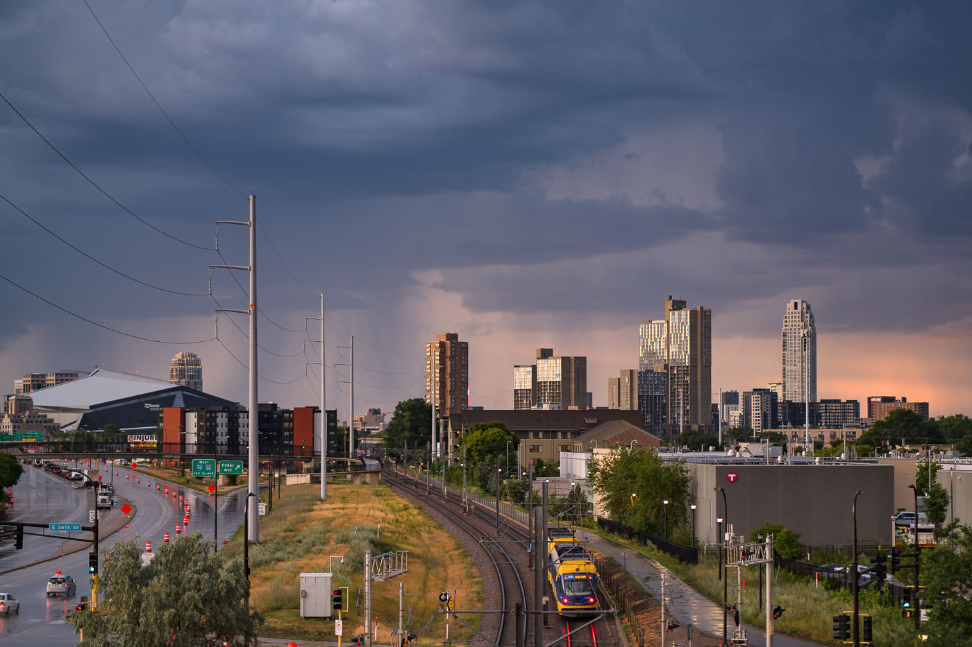 Storm clouds loom over the Minneapolis skyline on July 12, 2022, with the U.S. Bank Stadium visible on the left. The image also features the Metro Blue Line light rail, a key component of public transit in the Twin Cities. Opened in 2004, the Blue Line connects Minneapolis-Saint Paul International Airport and the Mall of America to downtown Minneapolis, serving as a vital link for commuters and visitors. The infrastructure facilitates access to the city's core employment centers and cultural attractions.