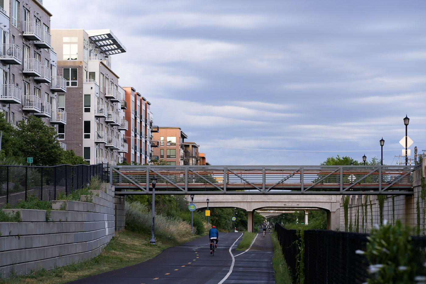 The Midtown Greenway in Minneapolis is a 5.5-mile-long trail developed on a former railroad corridor, providing a vital artery for cyclists and pedestrians through the city. Adjacent apartment buildings, constructed in recent years, demonstrate the integration of modern residential development with the trail's active use. A pedestrian bridge spans the greenway, connecting neighborhoods and enhancing access to this popular urban path.
