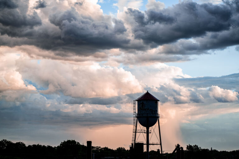 Roof Depot Water Tower Under Stormy Skies, Minneapolis 1 The Roof Depot water tower stands silhouetted against a dramatic sky in Minneapolis. Water towers like this one were essential for providing consistent water pressure to industrial and residential areas, particularly before the widespread adoption of modern pumping systems. This structure, likely built in the early to mid-20th century, served the needs of the surrounding industrial district. Its presence signifies a period of significant urban and industrial development in Minneapolis.