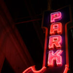 A classic vertical “PARK” marquee glows in red and magenta neon, marking one of downtown Minneapolis’s older parking structures that date back to the mid-20th century. These illuminated signs were once a staple of the city’s core, guiding drivers through the dense commercial grid before digital wayfinding and modern garages became standard. Many of these vintage markers survive as quiet architectural artifacts, attached to early high-rise buildings constructed during the postwar retail boom. Their hand-bent tubing and heavy steel housings reflect a period when neon craftsmanship was central to the city’s nighttime identity, especially along corridors near Nicollet Avenue, Hennepin Avenue, and the warehouse district.