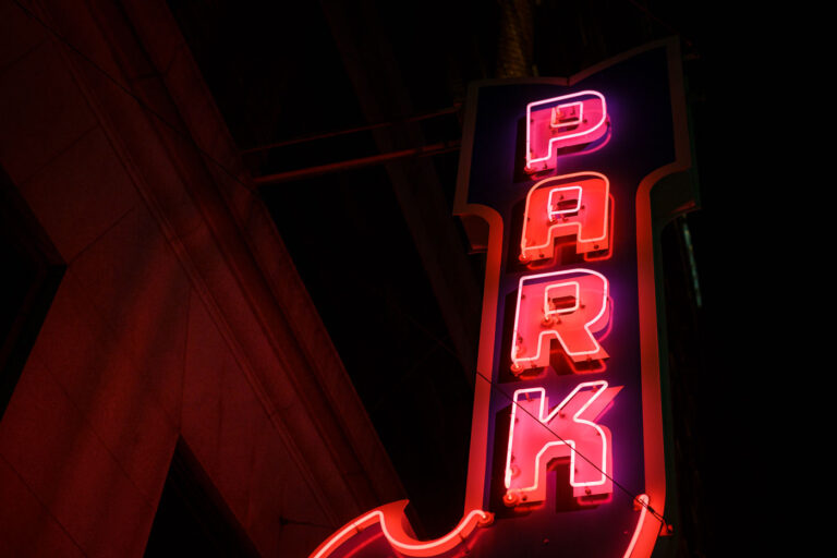 Vintage Neon “Park” Sign in Downtown Minneapolis 3 A classic vertical “PARK” marquee glows in red and magenta neon, marking one of downtown Minneapolis’s older parking structures that date back to the mid-20th century. These illuminated signs were once a staple of the city’s core, guiding drivers through the dense commercial grid before digital wayfinding and modern garages became standard. Many of these vintage markers survive as quiet architectural artifacts, attached to early high-rise buildings constructed during the postwar retail boom. Their hand-bent tubing and heavy steel housings reflect a period when neon craftsmanship was central to the city’s nighttime identity, especially along corridors near Nicollet Avenue, Hennepin Avenue, and the warehouse district.