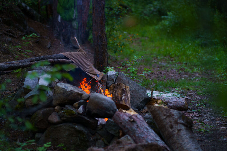 Superior National Forest Campfire, Minnesota 3 A campfire burns in a stone pit in Superior National Forest, Minnesota, with a towel draped over a log nearby. Smoke rises into the surrounding trees.