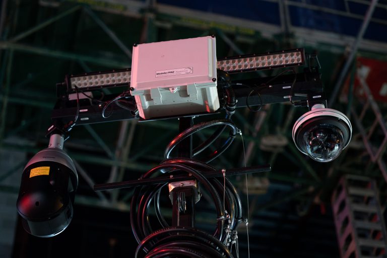 Surveillance Camera Rig on Construction Scaffolding 1 Dome and pan-tilt-zoom security cameras mounted on scaffolding at a construction site with LED light bars.