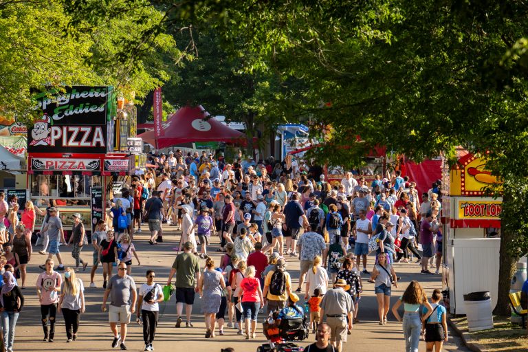 Spaghetti Eddie's Pizza Stand, Minnesota State Fairgrounds 4 Crowds fill a tree-lined avenue at the Minnesota State Fair, with a pizza vendor stand visible among the fairground attractions.