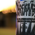 A flyer taped to a pole in downtown Minneapolis advertises a search for an “aggressive guitar player” and “people who give a damn,” echoing the recruitment style of 1980s metal bands. The poster lists influences ranging from Vixen and Madam X to Mötley Crüe, Poison, Ratt, and Judas Priest—names that shaped the Twin Cities’ hard-rock and glam-metal culture during the era of small clubs and independent bands. Its DIY design and bold typography reflect the ongoing tradition of grassroots music promotion that still surfaces in the city’s urban corridors.