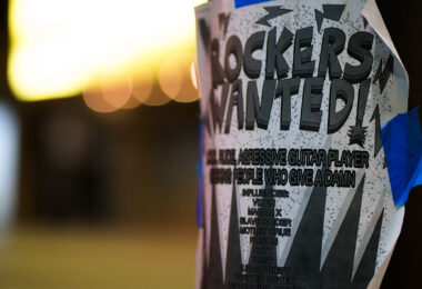 A flyer taped to a pole in downtown Minneapolis advertises a search for an “aggressive guitar player” and “people who give a damn,” echoing the recruitment style of 1980s metal bands. The poster lists influences ranging from Vixen and Madam X to Mötley Crüe, Poison, Ratt, and Judas Priest—names that shaped the Twin Cities’ hard-rock and glam-metal culture during the era of small clubs and independent bands. Its DIY design and bold typography reflect the ongoing tradition of grassroots music promotion that still surfaces in the city’s urban corridors.