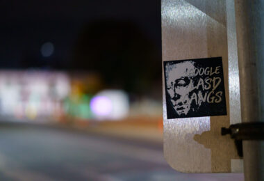 A sticker on a Minneapolis signpost references long-running allegations surrounding deputy “gangs” within the Los Angeles County Sheriff’s Department (LASD). Civil rights groups, journalists, and county oversight bodies have documented concerns for decades about informal deputy subgroups—some using matching tattoos or symbols—that critics say foster misconduct, retaliation, and internal loyalty structures.

Seeing a reference to those controversies on a street sign in Minneapolis reflects how national policing debates and accountability issues often circulate far beyond their place of origin, with artists and activists using stickers, posters, and small-scale street graphics to raise awareness or prompt online searches.