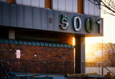 The address numbers 5001 hang damaged and partially peeled from the exterior of the former Southgate Office Tower in Bloomington, Minnesota. Shot during the late-afternoon winter light, the sign shows the wear of a building already deep into demolition. The brick façade, fencing, and scattered debris reflect the final stages of teardown at the long-vacant 1960s-era tower that once stood near I-494 and Portland Avenue.