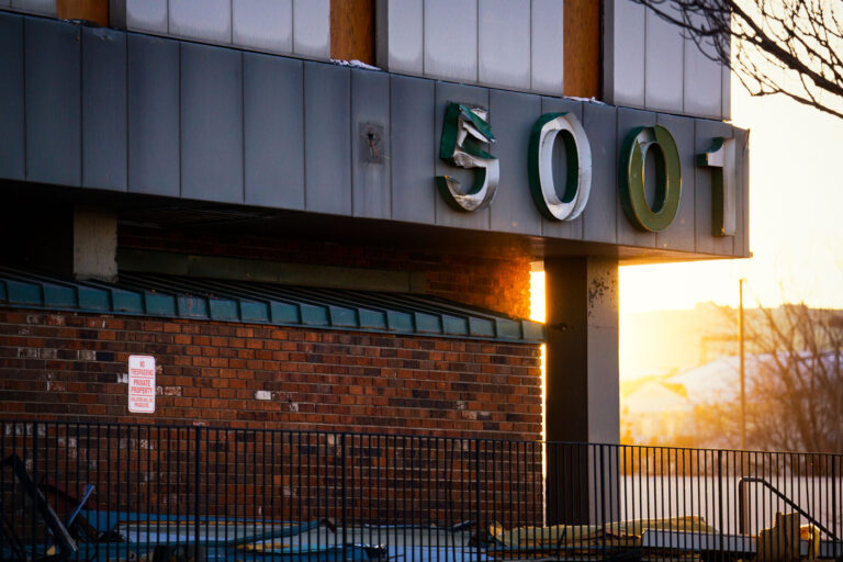 5001 Building During Southgate Demolition 4 The address numbers 5001 hang damaged and partially peeled from the exterior of the former Southgate Office Tower in Bloomington, Minnesota. Shot during the late-afternoon winter light, the sign shows the wear of a building already deep into demolition. The brick façade, fencing, and scattered debris reflect the final stages of teardown at the long-vacant 1960s-era tower that once stood near I-494 and Portland Avenue.