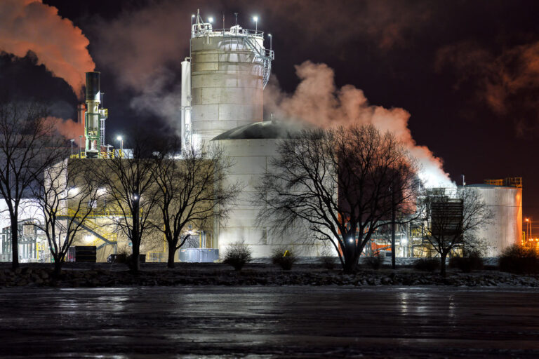 Green Bay Packaging Mill at Night 4 Green Bay Packaging’s modern recycled paper mill rises behind leafless winter trees along the Fox River in Green Bay, Wisconsin. The facility, completed in 2021 as one of the most advanced and energy-efficient mills in the country, emits illuminated plumes of steam that drift across the night sky. The river’s frozen surface reflects the mill’s lights and muted colors, creating a stark industrial winter landscape along the east bank of the Fox River.
