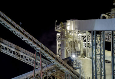 A detailed nighttime view of the conveyor towers and processing equipment at the Graymont lime plant in Green Bay, Wisconsin. The illuminated catwalks, ducts, and steel trusses highlight the facility’s continuous material-handling system, where crushed limestone moves through enclosed conveyors toward the plant’s kilns and storage silos. Fine dust, visible in the lights near the upper platforms, reflects the industrial character of a site that has served the region’s construction and manufacturing sectors for decades.