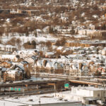 Winter Housing and Highway Corridor along I-94, Minneapolis 4 This view looks across the residential neighborhoods bordering Interstate 94 in Minneapolis, an area shaped heavily by mid-20th-century highway construction. When I-94 was built between the 1950s and early 1970s, it cut through several established communities—including parts of Cedar-Riverside, Seward, and Phillips—reshaping street grids, housing patterns, and long-standing cultural districts. The snow-covered homes clustered above the highway reflect a mix of older housing stock and later infill development that emerged after the corridor was completed. The elevated ramps and interchanges shown here connect local streets to one of the region’s primary east–west routes, linking downtown Minneapolis with St. Paul and the wider interstate system.