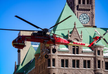 A heavy-lift Sikorsky S-64 Skycrane Helicopter in downtown Minneapolis bringing HVAC materials to the US Bank Plaza roof.