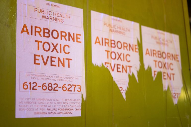 City of Minneapolis public health warning flyers about an airborne toxic event posted on a yellow wall.