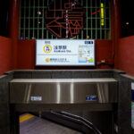 An entrance to Tokyo Metro’s Asakusa Station on the Ginza Line, marked with the station code G-19, leads commuters down a clean, tiled stairway under the red-painted gateway structure. The illuminated signage displays route maps and directional guidance, combining modern wayfinding with the surrounding area’s traditional aesthetic. Located near Sensō-ji Temple, this entrance reflects Asakusa’s balance of old Tokyo charm and contemporary transit design.