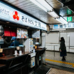 A small soba counter operates inside Asakusa Underground Street, one of Tokyo’s oldest surviving subterranean shopping arcades. Tucked beneath the streets near Asakusa Station, these compact eateries serve quick bowls of soba and udon to commuters and visitors moving between the metro and the surrounding neighborhood.

Opened in 1955, Asakusa Underground Street is considered the oldest underground shopping street in Japan. Its narrow corridors, low ceilings, and tightly packed storefronts preserve a postwar atmosphere that has largely vanished from Tokyo as major stations modernized. The passageway originally developed as a practical connection point for transit riders, but it evolved into a lively network of bars, snack counters, tobacconists, and small service shops. Today, despite gradual renovation, it remains one of the city’s most atmospheric relics of mid-20th-century urban life—an example of how Tokyo’s underground spaces doubled as both transportation infrastructure and neighborhood social hubs.