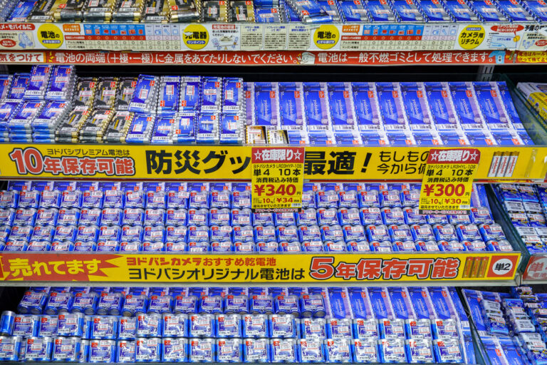 Battery Display at Yodobashi Camera Shinjuku 4 A densely stocked battery display inside Yodobashi Camera’s Shinjuku complex in March 2023. Yodobashi’s in-house battery line is prominently featured, with signage advertising long shelf-life options—10-year storage for premium models and 5-year storage for standard packs. Clear price labeling, bulk multi-pack options, and emergency-preparedness messaging reflect the store’s emphasis on reliability and daily-use electronics.Yodobashi Camera Shinjuku is one of Tokyo’s largest electronics hubs, spanning multiple buildings near the west exit of Shinjuku Station. Its battery aisles exemplify the retailer’s merchandising style: bright color-coded labels, multilingual product cues, and high-volume stock arranged for quick comparison by commuters and tourists alike.