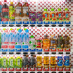 Drinks in a Tokyo Vending Machine 4 A brightly lit Japanese vending machine displays a meticulously arranged lineup of drinks—from Coca-Cola and Fanta to bottled teas, mineral waters, and Georgia coffee blends. Each row is clearly priced, some marked with blue “つめたい” (cold) or red “あったかい” (hot) labels, offering both chilled and warmed beverages. The right panel promotes the “Coke ON” smartphone app, merging tradition with tech-driven convenience. This snapshot captures Japan’s signature vending culture: accessible, efficient, and surprisingly aesthetic in its everyday precision.