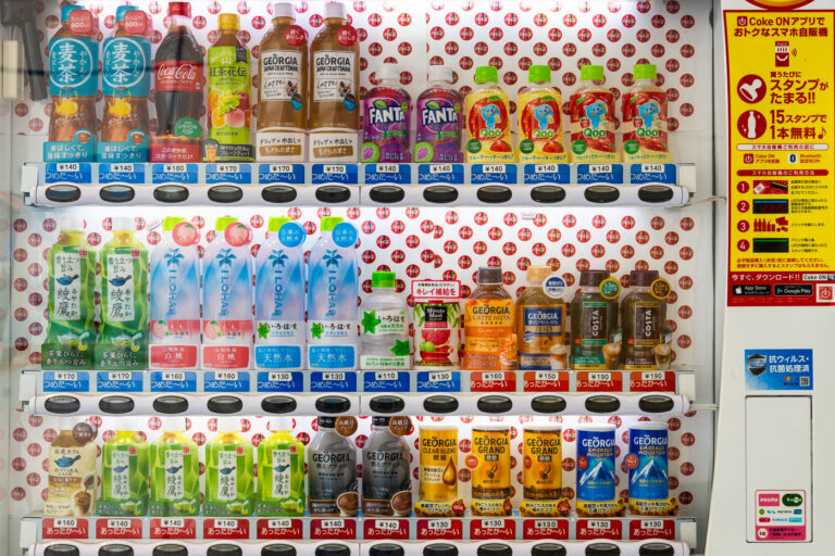 Drinks in a Tokyo Vending Machine 4 A brightly lit Japanese vending machine displays a meticulously arranged lineup of drinks—from Coca-Cola and Fanta to bottled teas, mineral waters, and Georgia coffee blends. Each row is clearly priced, some marked with blue “つめたい” (cold) or red “あったかい” (hot) labels, offering both chilled and warmed beverages. The right panel promotes the “Coke ON” smartphone app, merging tradition with tech-driven convenience. This snapshot captures Japan’s signature vending culture: accessible, efficient, and surprisingly aesthetic in its everyday precision.