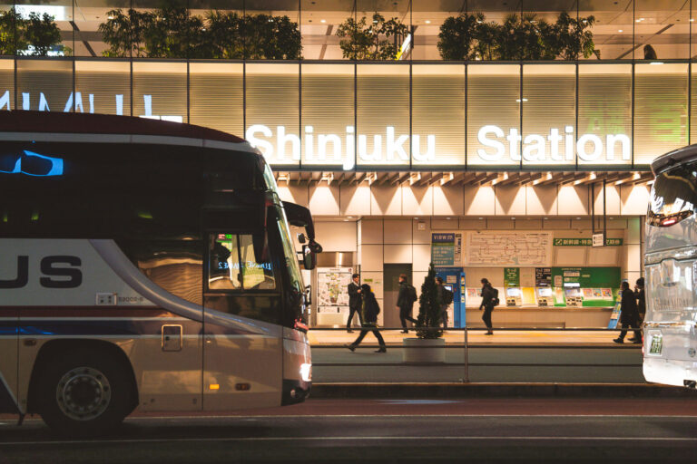 Evening Bus Terminal at Shinjuku Station 1 Intercity buses line up outside Shinjuku Station in Tokyo, one of the busiest rail hubs in the world and a major transfer point for long-distance coach services. The station’s west side is home to a dense cluster of express bus platforms that connect Tokyo with destinations across Honshu, Hokkaido, and Kyushu.Captured in March 2023, the photo shows the steady flow of evening commuters moving between the station concourse and the bus loading area, illuminated by the station’s modern façade lighting. The scene reflects Shinjuku’s role not only as a metropolitan transit hub but also as a key gateway for regional travel throughout Japan.