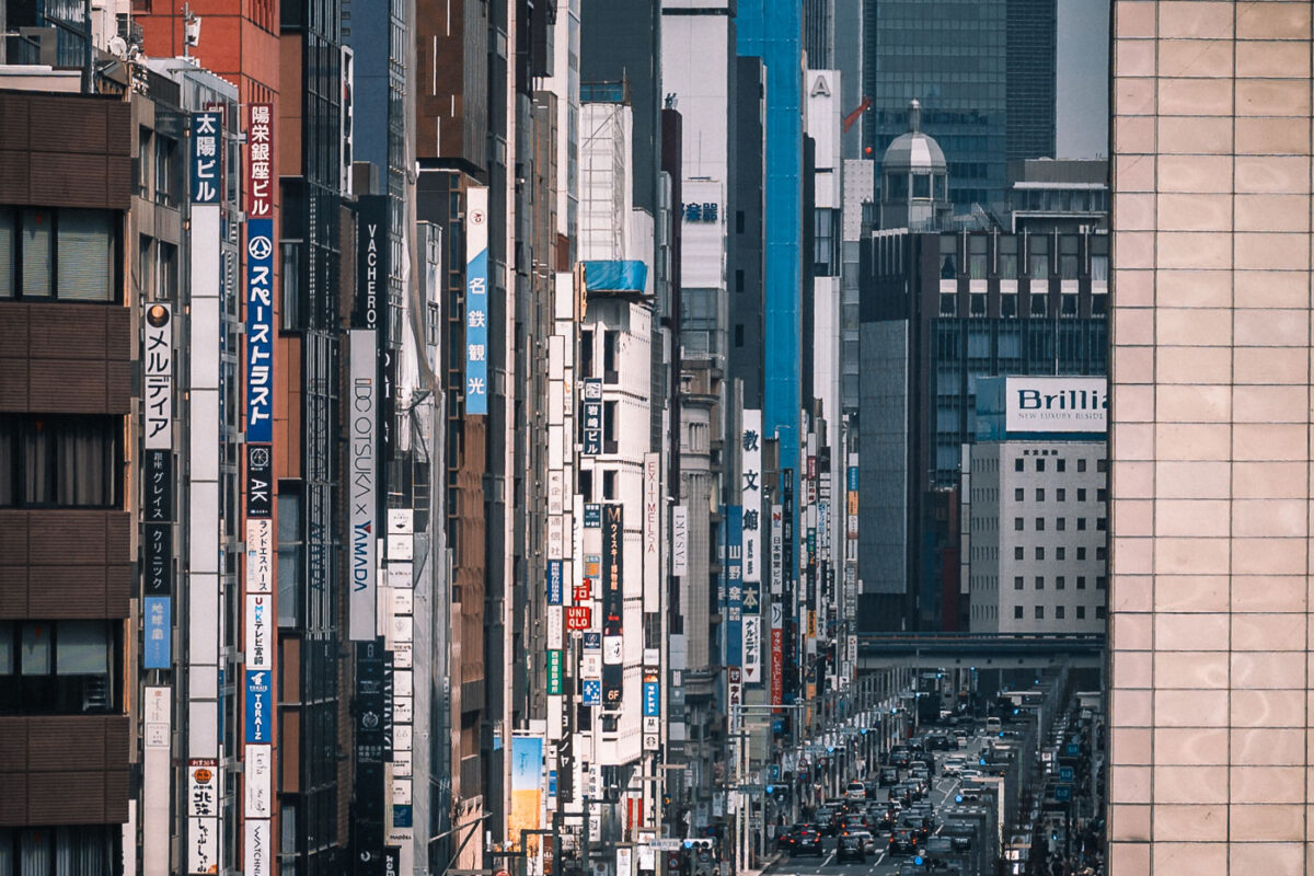 Vertical signs for businesses line the streets of Ginza, Tokyo, a major commercial district, with traffic visible on the road below.