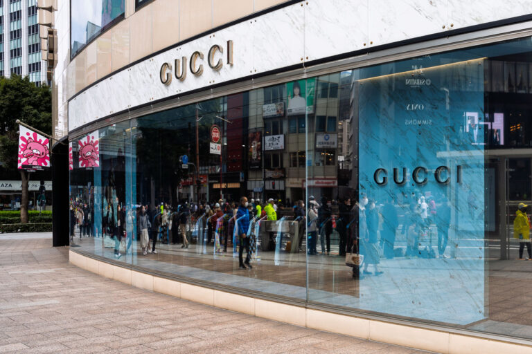 Reflections at Gucci Ginza 2 Marathon runners outside the Gucci flagship store in Tokyo’s Ginza district, their reflections merging with the pale blue marble of the storefront’s curved glass façade. The mirrored surface creates a layered composition — a city within a window — blending luxury retail architecture with the urban motion of shoppers and commuters. Behind the glass, soft interior lighting contrasts with the bustle outside, capturing a quiet tension between aspiration and reality. The scene evokes Ginza’s dual identity as both a symbol of global consumer culture and a distinctly Japanese streetscape, where design, commerce, and reflection coexist seamlessly.