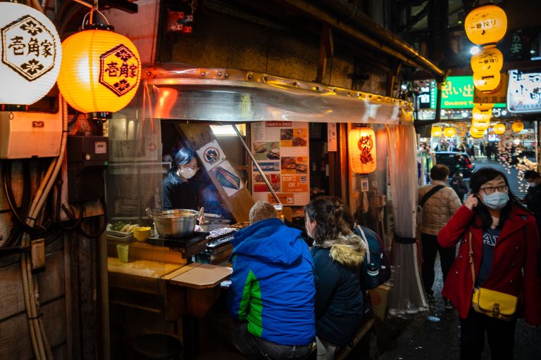 Ikkakuya Yakitori Stall, Omoide Yokocho, Shinjuku 1 Customers order food at a small Japanese street food stall decorated with yellow lanterns at night.