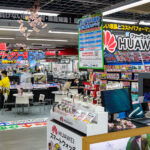 An interior view of Yodobashi Camera’s sprawling Shinjuku complex in March 2023, showing the densely organized electronics floor where computer hardware, mobile devices, and accessories are displayed under bold, color-saturated signage. The store’s characteristic layout—aisles packed with laptops, desktop components, peripherals, and promotional displays—reflects its role as one of Tokyo’s most comprehensive electronics retailers.

Prominent branding for Huawei laptops and smartwatches fills the foreground, while the surrounding aisles feature comparative pricing banners, point-reward offers, and emergency power supply promotions. Yodobashi Camera’s Shinjuku location spans multiple interconnected buildings near the west exit of Shinjuku Station, drawing commuters, hobbyists, and tourists with its high inventory turnover, product variety, and multilingual support.