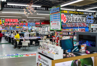 An interior view of Yodobashi Camera’s sprawling Shinjuku complex in March 2023, showing the densely organized electronics floor where computer hardware, mobile devices, and accessories are displayed under bold, color-saturated signage. The store’s characteristic layout—aisles packed with laptops, desktop components, peripherals, and promotional displays—reflects its role as one of Tokyo’s most comprehensive electronics retailers.

Prominent branding for Huawei laptops and smartwatches fills the foreground, while the surrounding aisles feature comparative pricing banners, point-reward offers, and emergency power supply promotions. Yodobashi Camera’s Shinjuku location spans multiple interconnected buildings near the west exit of Shinjuku Station, drawing commuters, hobbyists, and tourists with its high inventory turnover, product variety, and multilingual support.