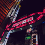 The iconic illuminated gate marking Kabukichō Ichiban-gai, photographed in Shinjuku, Tokyo. Installed in the late 1960s and redesigned several times since, the red archway has become one of the most recognizable entrances to Tokyo’s largest entertainment district.

Kabukichō developed after World War II as a planned theater district—its name comes from a never-built kabuki theater—before evolving into a dense zone of restaurants, bars, cinemas, and nightlife venues. The gate’s bright bulbs and bold lettering serve as a symbolic threshold into the neighborhood’s tightly packed streets, which remain active late into the night.