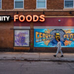 A man walks in front of the George Floyd mural on the side of "Unity Foods". Unity Foods was formerly named Cup Foods.