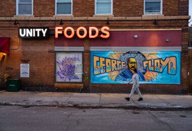 A man walks in front of the George Floyd mural on the side of "Unity Foods". Unity Foods was formerly named Cup Foods.
