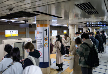Commuters wait for the next train on the Tokyo Metro Ginza Line, Japan’s oldest underground subway line and one of the city’s most heavily traveled routes. This platform—serving trains toward Toranomon, Akasaka-mitsuke, Omote-sando, and Shibuya—captures a typical weekday scene with riders lining up at designated doors, phones in hand, as screen doors stand ready to open with the arriving train.

Opened progressively between 1927 and 1939, the Ginza Line was Asia’s first subway, modeled after London’s Underground and New York’s early lines. Its development helped shape modern Tokyo by linking emerging commercial districts—including Asakusa, Ginza, and Shibuya—into a cohesive urban network. Today, despite being nearly a century old, the line remains a backbone of the city’s transportation system, continually upgraded with platform doors, advanced signaling, and refreshed stations to meet the demands of one of the world’s busiest transit cities.