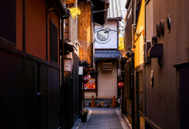 A narrow side alley branching off Hanamikoji-dori in Kyoto’s Gion district, photographed in March 2023. This historic area is known for its preserved machiya townhouses—traditional wooden buildings that date back to the Edo and Meiji periods and once served as both residences and storefronts for merchants and artisans. Many of the structures visible here retain their classic features, including wooden latticework (koshi), earthy plaster walls, deep-eaved roofs, and lanterns marking the entrances of small eateries and teahouses.

Hanamikoji-dori remains closely associated with Kyoto’s hanamachi culture, where geiko and maiko still work in nearby teahouses. While the main street draws steady foot traffic, the smaller lanes behind it—like the one pictured—capture the quieter, more atmospheric side of Gion, where the scale of the architecture narrows and the district’s centuries-old urban fabric becomes especially clear.