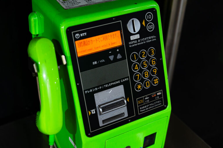 NTT Pay Phone In Japan 1 A bright green NTT public payphone, once a fixture of every Japanese street corner and train station, stands as a reminder of Japan’s pre-smartphone era. Its sturdy metal receiver, telephone card slot, and bilingual instructions highlight the country’s enduring attention to accessibility and precision. Still functional today, these phones remain a quiet symbol of Japan’s blend of reliability and retro technology.