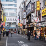 Sanbangai Street sits just west of Shinjuku Station and is part of the dense network of narrow commercial lanes that define this section of the city. The area developed rapidly after the mid-20th-century reconstruction of Shinjuku and is now lined with small restaurants, curry shops, bars, and specialty eateries catering to commuters and office workers moving through the station district each day.

The nearby Shinjuku Post Office has long served as a recognizable landmark on the north side of the station, anchoring a neighborhood known for its mix of long-established storefronts and constantly rotating food businesses.