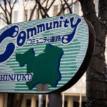 An older enamel “Community Road” sign in Shinjuku, Tokyo, photographed in March 2023. These signs—marked with コミュニティ道路 (“community road”) and a stylized map of the ward—were installed beginning in the late 1970s and 1980s as part of a municipal effort to identify quieter local streets prioritized for pedestrians, schools, and neighborhood traffic rather than through-traffic.

Although many have faded or disappeared as Shinjuku redeveloped, surviving signs like this one remain a small reminder of earlier phases of the ward’s streetscape planning. The hand-drawn lettering, green stripes, and simplified ward outline reflect the graphic design style common in Tokyo’s municipal signage of that era.